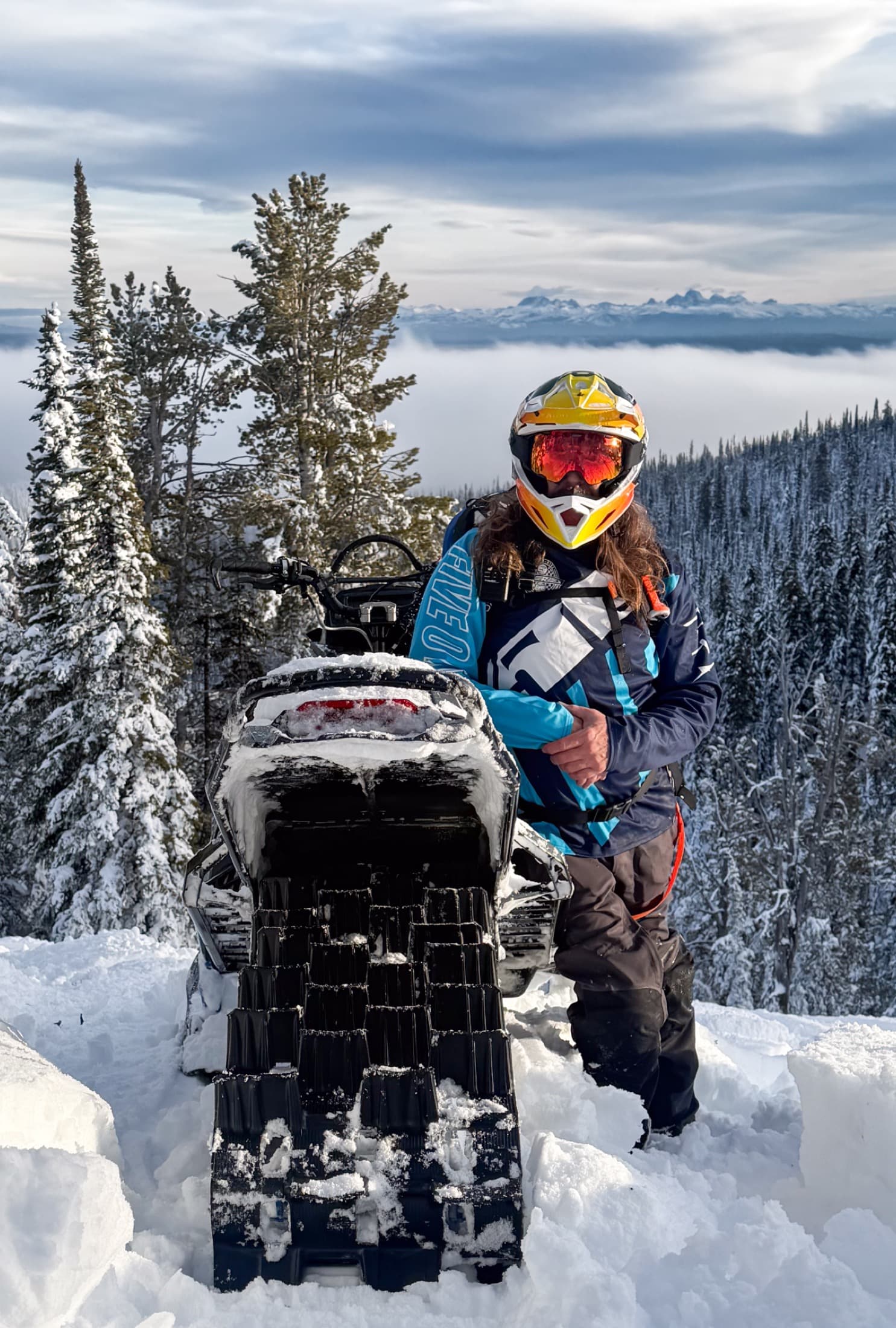 Snowmobiler at a snowy overlook with the Tetons in the distance